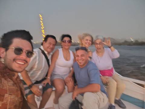       Blurry dusk selfie of six travelers laughing on a small Nile boat with festive lights
  
