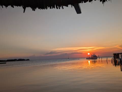       Serene sunset over calm Caribbean waters with a boat anchored near the glowing horizon.
  