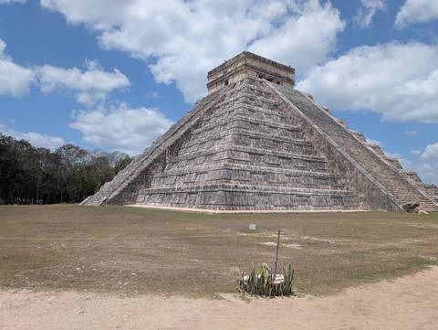       The massive stone pyramid of El Castillo at Chichén Itzá stands under scattered clouds.
  