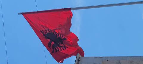       Bright red Albanian flag with black double-headed eagle waving against clear blue sky
  