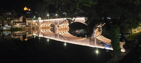       Night scene of an illuminated arched stone bridge perfectly reflected on a calm river
  