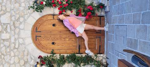       Young woman playfully posing in front of a rustic wooden door framed by red roses
  
