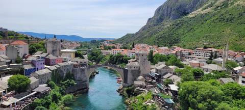      Classic postcard view of Mostar's Old Bridge arching over emerald Neretva River amid orange rooftops
  