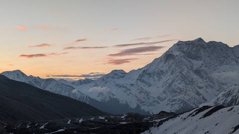       Snow-clad Himalayan peaks under soft pastel clouds at dusk over a remote valley.
  