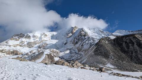       Massive snow-covered Himalayan face rising into a clear deep blue sky with drifting cloud.
  
