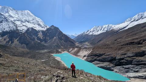       Hiker overlooking striking turquoise glacial lake set amid dramatic snow-capped Himalayan ranges.
  