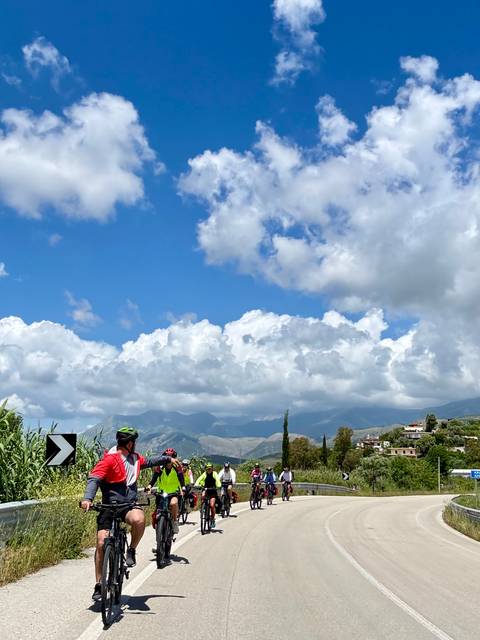       Solo cyclist pauses on a countryside road with dramatic cloud-filled sky and distant hills.
  