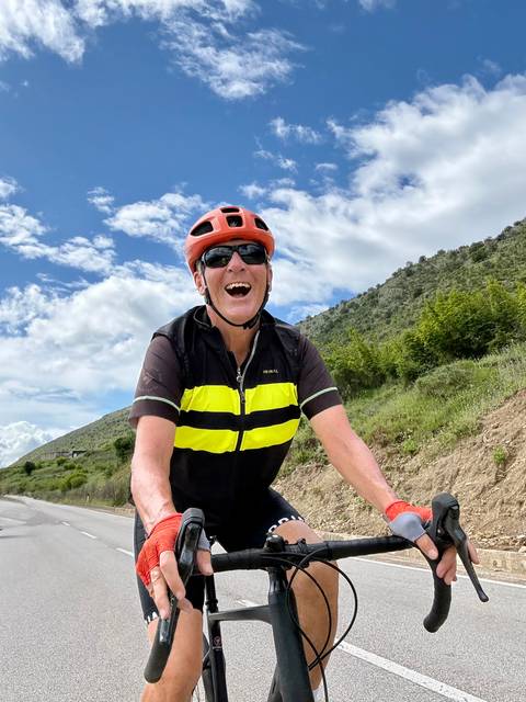       Close-up portrait of a happy cyclist wearing a helmet and sunglasses riding uphill.
  