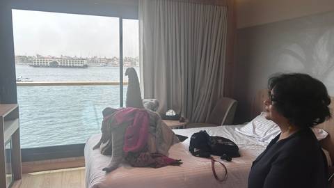       Cruise cabin with a woman looking out over the Nile where another ship passes by
  