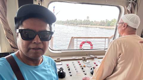       Selfie on the bridge of a Nile cruise boat with palm-lined riverbank in background
  