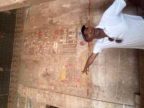       Egyptian guide pointing out colorful wall reliefs inside an ancient temple
  