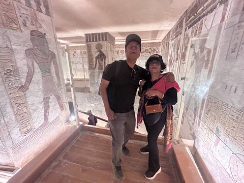       Visitors pose inside a dimly lit Egyptian tomb corridor covered in hieroglyphs
  
