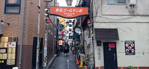       Entrance arch to Shinjuku Golden Gai’s narrow alley lined with bars and sticker-covered walls.
  