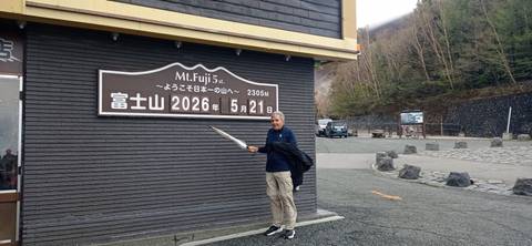       Traveller posing with umbrella beside the elevation sign at Mount Fuji’s 5th Station.
  