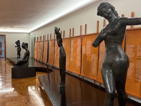       Art gallery interior with bronze sculptures and walls lined with descriptive orange panels.
  