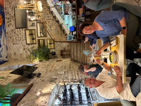       Smiling couple toast glasses of wine inside a cozy stone-walled Croatian restaurant.
  
