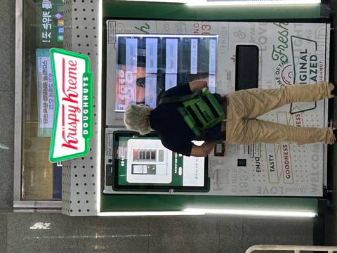       Man using a Krispy Kreme doughnut vending machine in a station
  