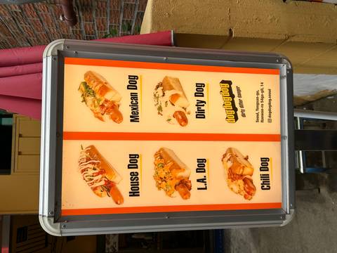       Menu signboard displaying various gourmet hot dogs on a city street
  