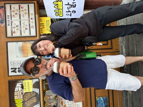       Two people happily sharing iced drinks at a street stall with Korean signs
  