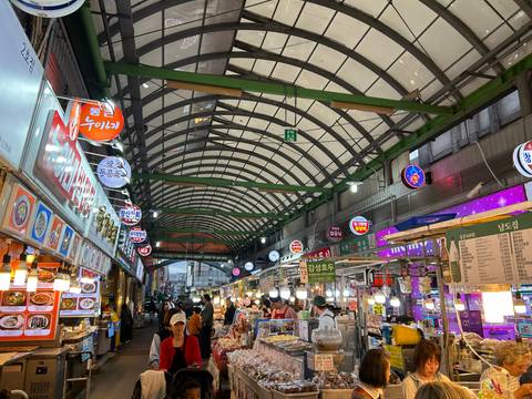       Bustling covered food market with neon signs, vendor stalls and diners in Seoul
  