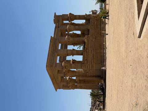       View of Philae Temple’s sandstone colonnade against a clear blue Egyptian sky.
  