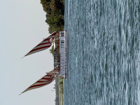       Traditional white Nile sailing boat with red-striped lateen sails glides across wide blue water.
  