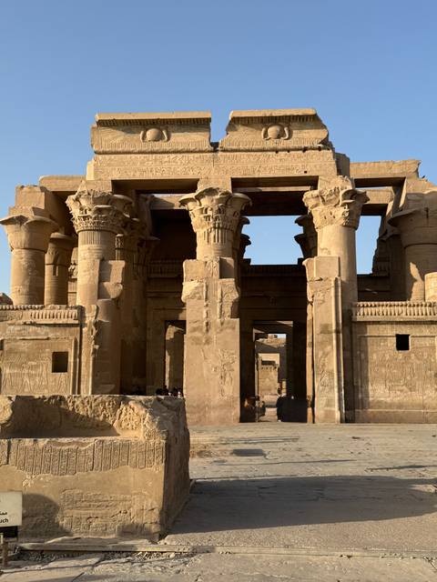       Sunlit sandstone columns and reliefs of Kom Ombo Temple with visitors exploring the ruins.
  