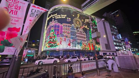       Vibrant Christmas-themed light display wraps a city building on a busy Seoul street at night.
  