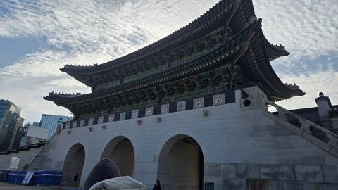       Majestic stone Gwanghwamun-style gate with ornate green roof tiles silhouetted against a textured sky.
  
