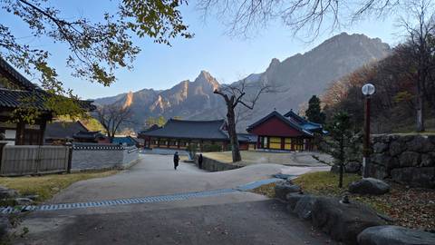       Mountain temple complex nestled beneath rugged peaks at dawn light with visitors strolling the courtyard.
  