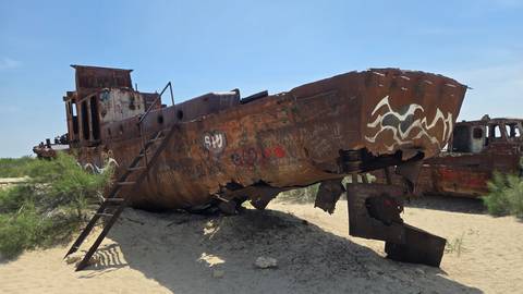       Rusting fishing vessel lies beached on desert sands at the Aral Sea ship graveyard.
  