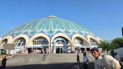       Domed Chorsu Bazaar in Tashkent displays intricate blue-green tile patterns above busy steps.
  
