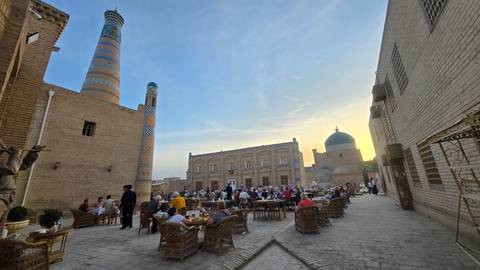       Courtyard café fills with diners at sunset beneath Khiva’s distinctive minarets.
  