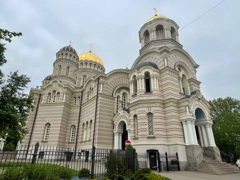       Ornate Orthodox cathedral with striped brickwork and golden dome against grey sky.
  