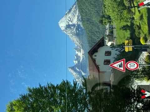       Village house with alpine backdrop and road signs in foreground on sunny day.
  