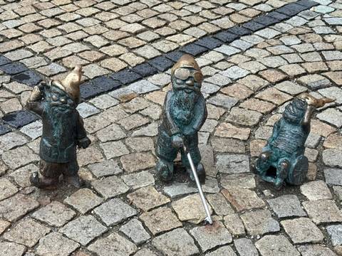       Three bronze dwarf statues on cobblestone pavement.
  