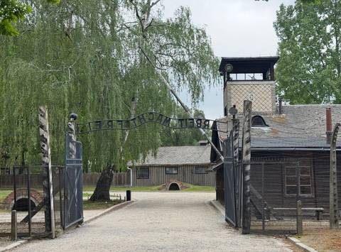       Arched 'Arbeit macht frei' gate at Auschwitz with guard tower in background.
  