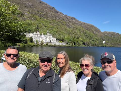       Group posing with Kylemore Abbey across the lake on a bright sunny day.
  