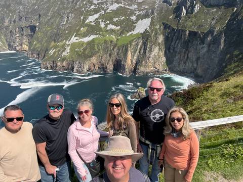       Group standing at a high ocean cliff lookout with dramatic waves and headlands below.
  