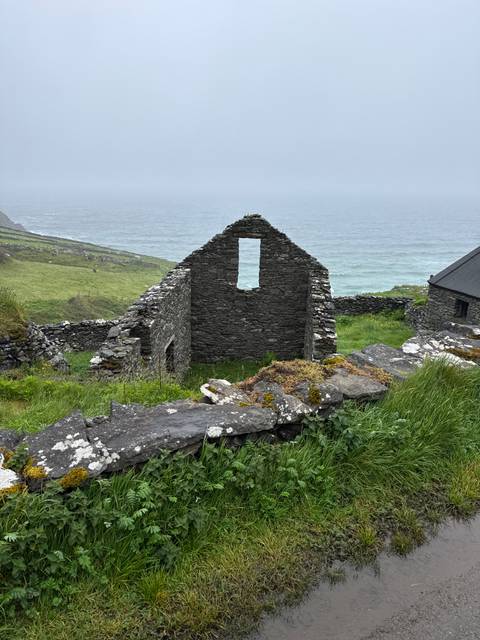       Stone ruin of a roofless cottage overlooking green cliffs and the Atlantic Ocean under misty skies.
  