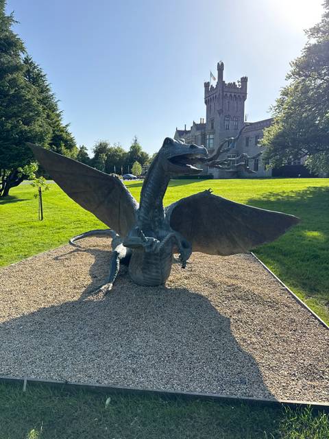       Large bronze dragon statue with outstretched wings displayed on gravel in front of a manor lawn.
  