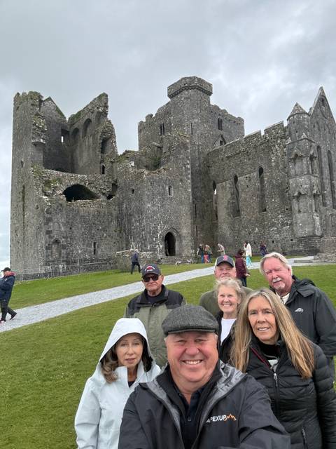       Small tour group posing happily in front of the medieval ruins of the Rock of Cashel.
  
