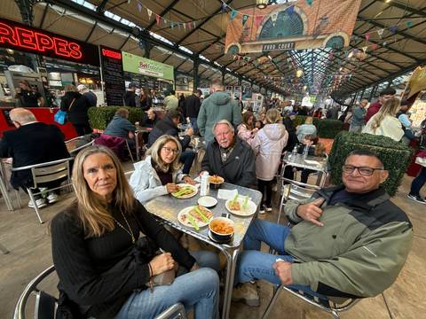       Friends enjoying lunch at a bustling indoor market food court with rows of stalls and diners.
  