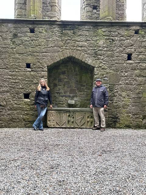       Couple posing on either side of a medieval stone fountain within a ruin courtyard.
  
