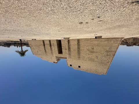       Massive sandstone pylon of Medinet Habu Temple standing alone against a cloudless blue sky.
  