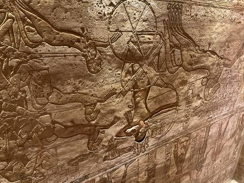       Close-up of a detailed ancient Egyptian wall relief showing a chariot scene carved in sandstone.
  