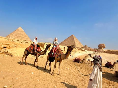       Tourists riding camels in front of the Pyramids and the Sphinx in the desert
  