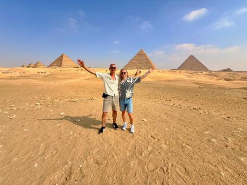       Happy couple posing with arms raised before the Great Pyramids in the sandy desert
  