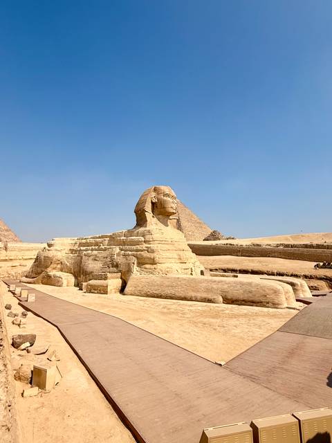       Close-up view of the Great Sphinx with a pyramid and blue sky behind
  