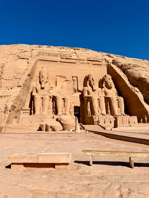       Massive seated statues carved into the façade of Abu Simbel temple under clear sky
  